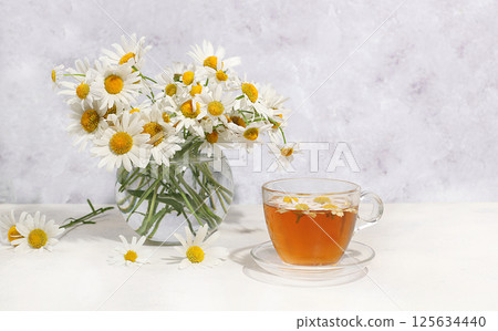 Chamomile tea in a transparent cup with natural small chamomile flowers on a light table, the concept of herbal tea and proper natural nutrition, selective focus 125634440