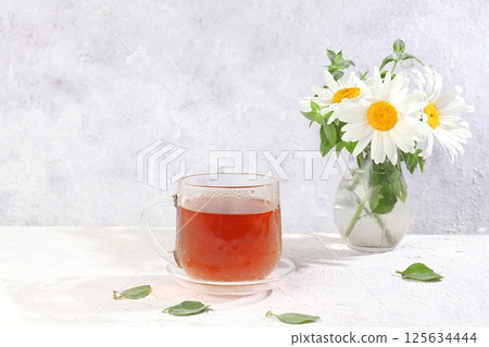 Chamomile tea in a transparent cup with natural small chamomile and mint flowers on a light sunny table, the concept of herbal tea and proper natural nutrition, promote weight loss, selective focus Chamomile tea in a transparent cup with natural small chamomile and mint flowers on a light sunny table, the concept of herbal tea and proper natural nutrition, promote weight loss, selective focus 125634444