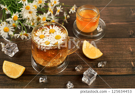 Chamomile tea with lemon in transparent glasses with natural small chamomile flowers on a rustic table, concept of medicinal herbal tea and proper natural nutrition, summer card, 125634453