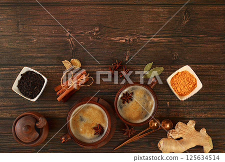 Indian masala chai tea with milk, ginger, anise and cinnamon on an old wooden table. Traditional drink with spices, cafe concept, advertising for restaurant and menu. Selective focus Indian masala chai tea with milk, ginger, anise and cinnamon on an old wooden table. Traditional drink with spices, cafe concept, advertising for restaurant and menu. Selective focus 125634514