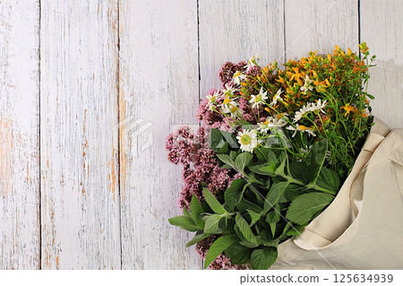 A flower arrangement of wild medicinal herbs on a wooden table in a canvas eco-friendly bag, a bouquet of St. John's wort, oregano, mint, chamomile, a collection of useful herbs for treatment . 125634939