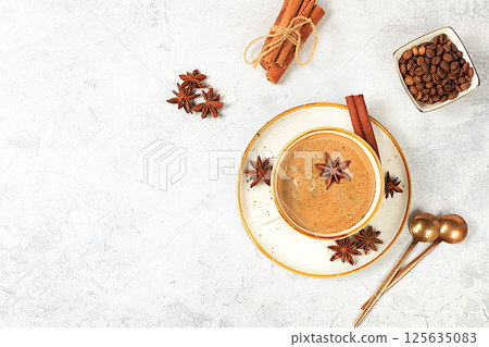 Cup of coffee with milk, ginger, anise and cinnamon on an old concrete table. Traditional Indian drink with spices, cafe concept, advertising for restaurant and menu. Selective focus 125635083