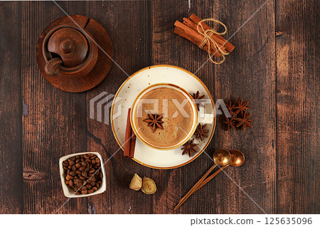 Cup of coffee with milk, ginger, anise and cinnamon on an old wooden table. Traditional Indian drink with spices, cafe concept, advertising for restaurant and menu. Selective focus 125635096