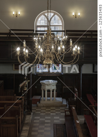 Stunning view of Chandelier hanging from the ceiling over The white octagonal baptismal font inside of The Church of King Charles the Martyr. Stunning view of Chandelier hanging from the ceiling over The white octagonal baptismal font inside of The Church of King Charles the Martyr. 125635493