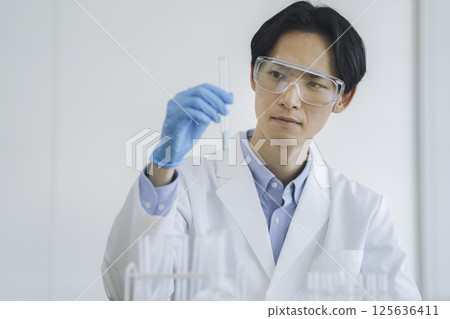 A man in a white coat working with a test tube, experiment image 125636411