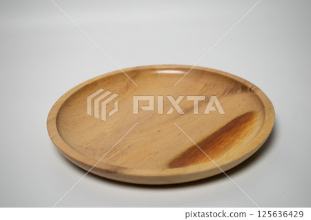A round wooden plate with a smooth finish, placed on a white background. 125636429
