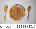 A wooden spoon, plate, and fork set on a white background, arranged neatly for a natural dining setup. 125636518