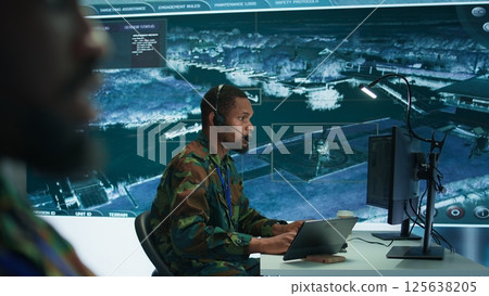Soldiers in a modern command center analyze live data from cctv radar sources, satellite feeds and surveillance systems. Intelligence to support strategic planning and military operations. Camera B. 125638205