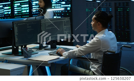 Person with disability in inclusive high tech server room facility ensuring data remains shielded from threats. Wheelchair user protecting data center hardware equipment, camera A 125638207