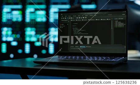 Close up of code running on laptop screen in data center used for managing gear energy consumption. Focus on notebook used by software developer in blurry background in server farm, camera A 125638236