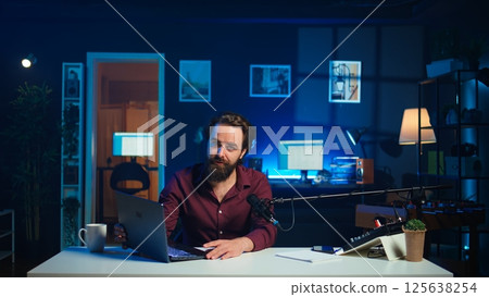 Influencer in studio endorsing laptop from brand sponsoring video, talking in microphone. Content creator does influencer marketing by promoting notebook, recording with high tech mic, camera B Influencer in studio endorsing laptop from brand sponsoring video, talking in microphone. Content creator does influencer marketing by promoting notebook, recording with high tech mic, camera B 125638254