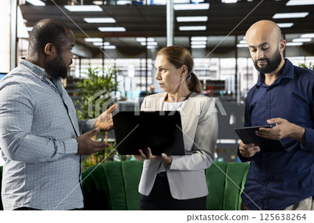 Multiracial workers using laptop device to write emails, solving tasks. Staff members typing on notebook keyboard in office, making sure documents are quality assurance compliant Multiracial workers using laptop device to write emails, solving tasks. Staff members typing on notebook keyboard in office, making sure documents are quality assurance compliant 125638264