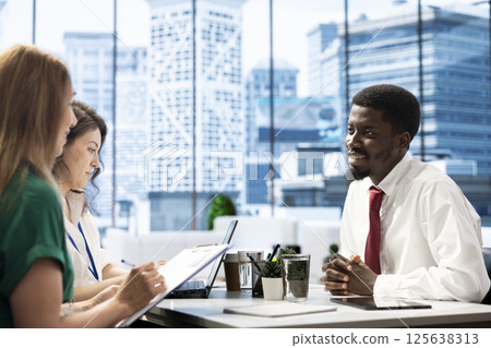 Human resources team looking at african american man CV, sitting at office desk. HR department staff members selecting candidates to work for company, reading person resume 125638313