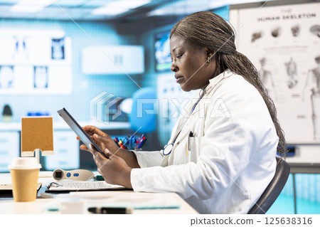 Black physician providing checkup examination on insurance with patient, employing technology for diagnostic tools in clinic. Man asking medic about wellness advice, recovery plan. 125638316