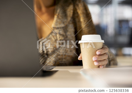 Successful woman in her workplace manages a variety of business tasks, drinking her morning coffee. Administrator focuses on business development, reports and project deadline. Close up. Successful woman in her workplace manages a variety of business tasks, drinking her morning coffee. Administrator focuses on business development, reports and project deadline. Close up. 125638336