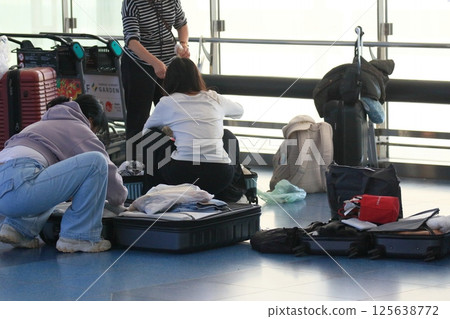 Foreign tourists packing their suitcases in the airport departure lobby 125638772