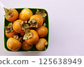 Bunch of ripe persimmons lies in a square green bowl on a white table. Top view 125638949