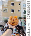 Pumpkin carved for Halloween on a man outstretched hand in front of a building 125638955
