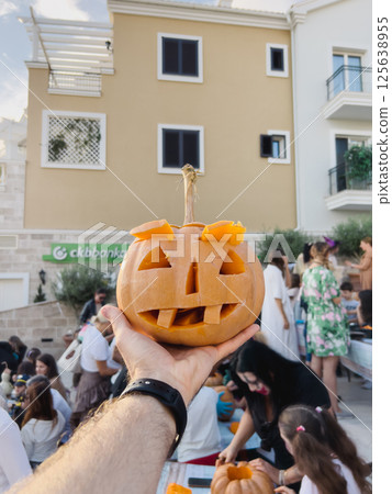 Pumpkin carved for Halloween on a man outstretched hand in front of a building Pumpkin carved for Halloween on a man outstretched hand in front of a building 125638955
