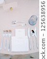Personalized invitation lies in a white napkin on the table next to the cutlery, opposite a blank card on a stand 125638956