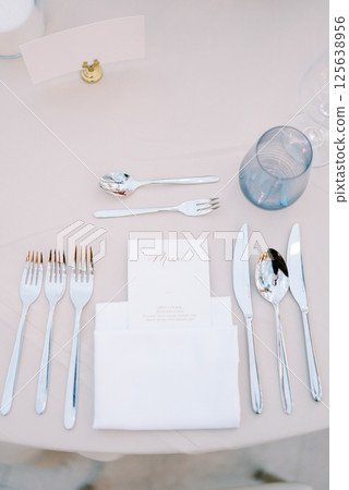 Personalized invitation lies in a white napkin on the table next to the cutlery, opposite a blank card on a stand 125638956
