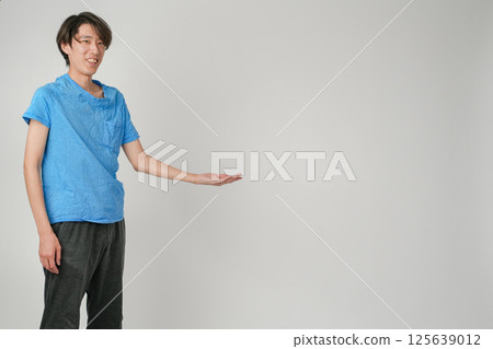 一位身穿藍色襯衫和黑色慢跑褲的日本男子看著我,微微一笑,將左手指向腰部上方,指著某個東西。 一位身穿藍色襯衫和黑色慢跑褲的日本男子看著我,微微一笑,將左手指向腰部上方,指著某個東西。 125639012