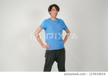 A man with his arms on his hips, his body tilted slightly, looking cool and wearing glasses as he stares at us. A man with his arms on his hips, his body tilted slightly, looking cool and wearing glasses as he stares at us. 125639019