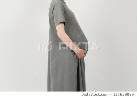 A woman who is 10 months pregnant and about to give birth supports her large belly with both hands. 125639089