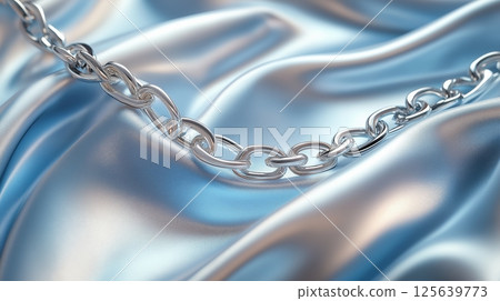 Elegant silver chain draped on soft blue satin fabric during daytime 125639773