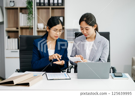 Businesswomen work and discuss their business plans. A women employee explains and shows her colleague in office. 125639995