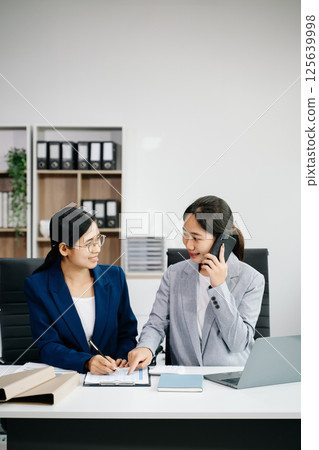 Businesswomen work and discuss their business plans. A women employee explains and shows her colleague in office. Businesswomen work and discuss their business plans. A women employee explains and shows her colleague in office. 125639998