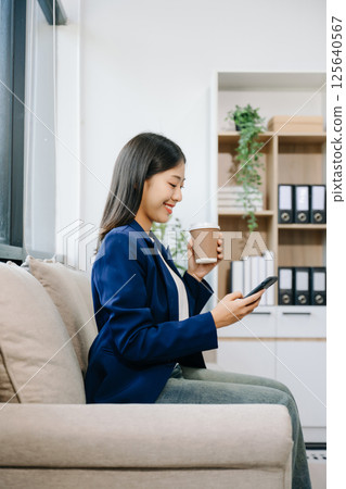 Young asian woman relax on comfortable couch at home texting messaging on smartphone and tablet 125640567