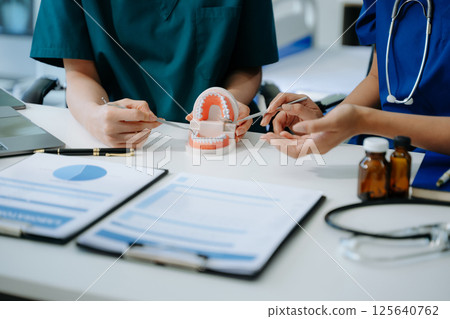 Concentrated dentist sitting at table with jaw samples tooth model and working with tablet and laptop in dental office Concentrated dentist sitting at table with jaw samples tooth model and working with tablet and laptop in dental office 125640762