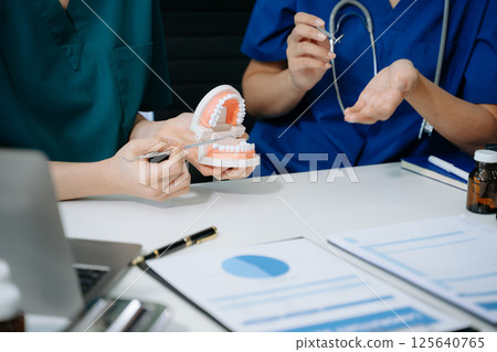 Concentrated dentist sitting at table with jaw samples tooth model and working with tablet and laptop in dental office 125640765