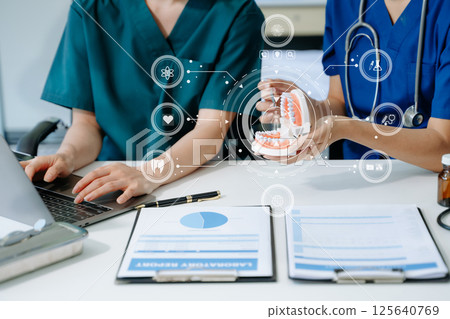 Dentist sitting at table with jaw samples tooth model and working with tablet and laptop in dental modern office Dentist sitting at table with jaw samples tooth model and working with tablet and laptop in dental modern office 125640769