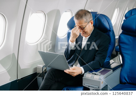 Photo of a frustrated senior man sitting on an airplane with her head in her hands. 125640837