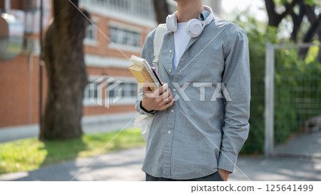 Close up of a man holding books and smartphone in right hand while standing hand in pocket on street 125641499