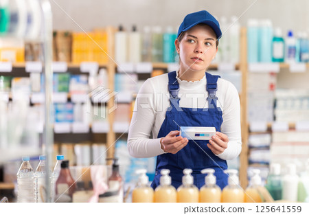 In sales area of pharmacy, builder woman examines packaging of gel for burns In sales area of pharmacy, builder woman examines packaging of gel for burns 125641559
