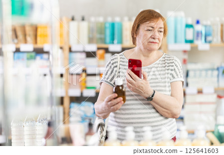 Senior woman in pharmacy scans QR code on antitussive syrup Senior woman in pharmacy scans QR code on antitussive syrup 125641603