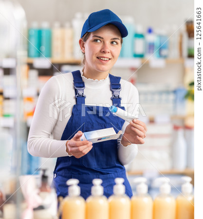 In sales area of pharmacy, builder woman examines packaging of gel for burns In sales area of pharmacy, builder woman examines packaging of gel for burns 125641663