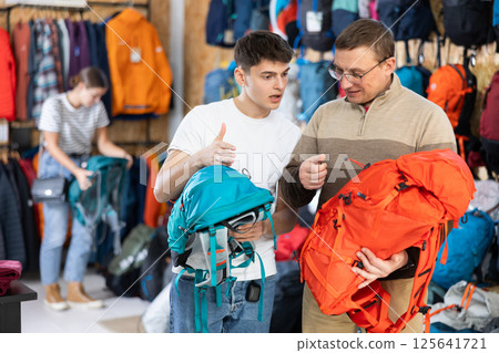 Father and son choose a backpack for hike together in store that sells sports equipment Father and son choose a backpack for hike together in store that sells sports equipment 125641721