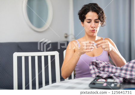 Woman sewing button on shirt sleeve at home Woman sewing button on shirt sleeve at home 125641731