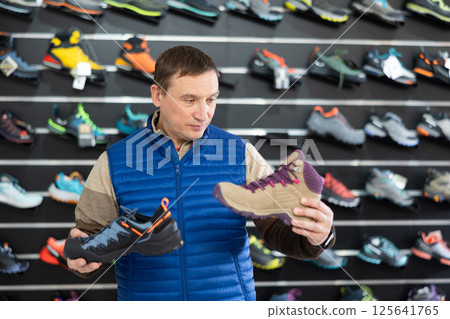 Attentive male athlete chooses sports winter shoes for hiking in sports store 125641765