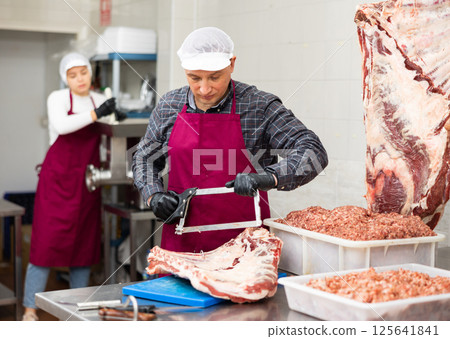 Butchery worker sawing beef ribs at cutting table Butchery worker sawing beef ribs at cutting table 125641841