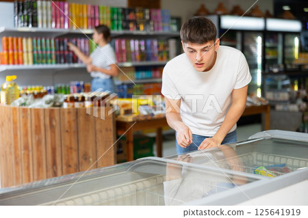 Guy chooses frozen semi-finished products in supermarket Guy chooses frozen semi-finished products in supermarket 125641919