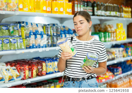 Young girl stands in cereal section of supermarket and chooses pack of peas 125641938