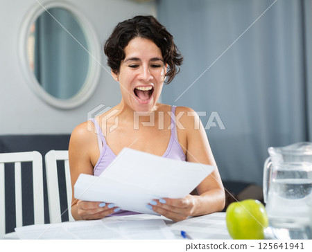 Brunette woman reading letter while sitting at table at home 125641941
