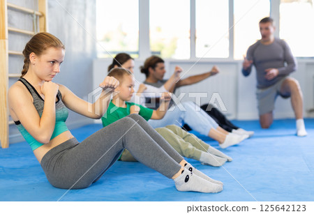 Group of people performing combat strikes sitting during group training 125642123