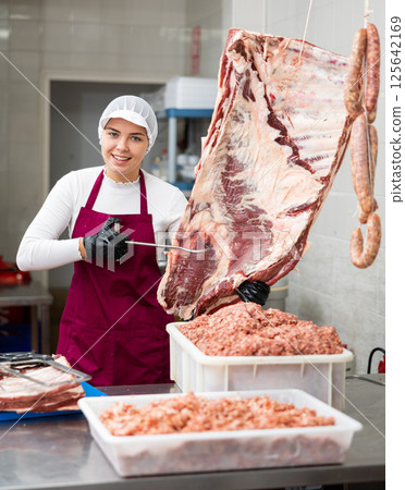 Happy female butcher showing big piece of beef ribs in meat section of supermarket 125642169