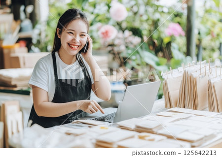 Young business owner multitasking happily while taking phone call in a vibrant workspace 125642213